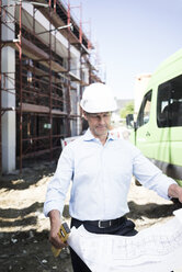 Architect with blueprint wearing hard hat on construction site - MOEF01299