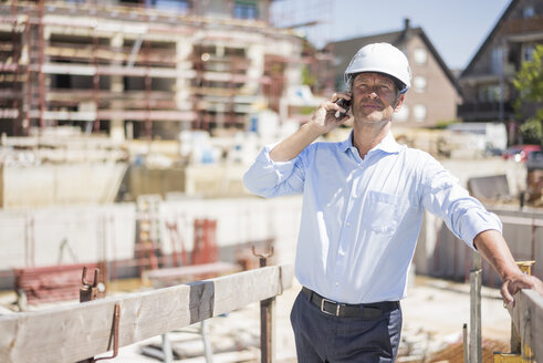 Mann mit Schutzhelm telefoniert auf einer Baustelle - MOEF01306