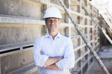 Porträt eines selbstbewussten Mannes mit Schutzhelm auf einer Baustelle - MOEF01311