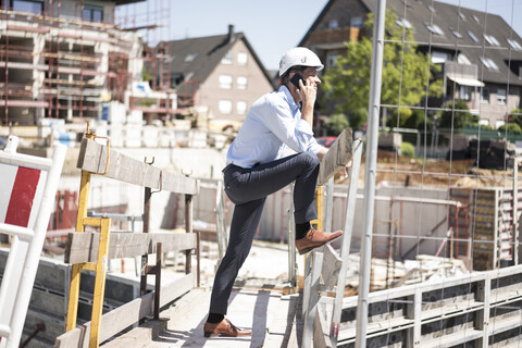 Mann mit Schutzhelm telefoniert auf einer Baustelle, lizenzfreies Stockfoto