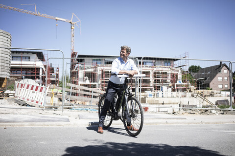 Mann mit E-Bike auf einer Baustelle und schaut sich um, lizenzfreies Stockfoto