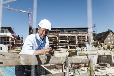 Mann mit Schutzhelm benutzt Mobiltelefon auf einer Baustelle - MOEF01328