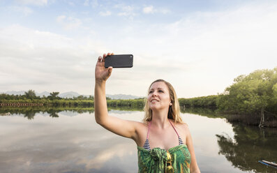 Junge Frau macht Smartphone-Selfie vor einem See, Gili Meno, Lombok, Indonesien - CUF23007