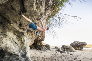 Male free climber climbing rock overhang on Pandawa Beach, Bali, Indonesia - CUF23012