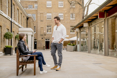Junger Mann begrüßt seine Freundin auf einer Bank sitzend, Kings Road, London, UK - CUF23068