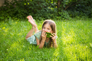 Portrait of little girl lying on a meadow eating watermelon - LVF07035