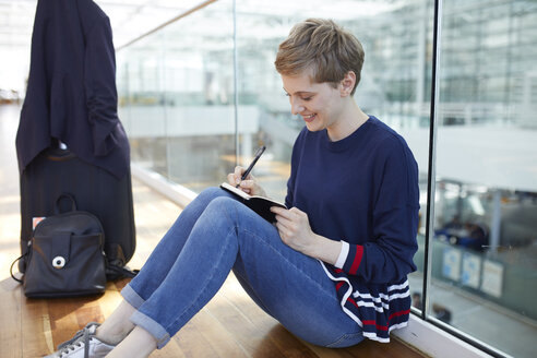 Blond businesswoman sitting on ground, writing in notebook - PNEF00704