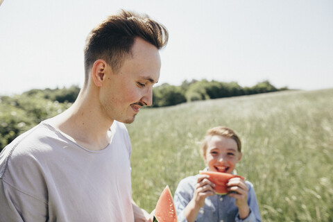Glücklicher junger Mann und Junge auf einem Feld, die Wassermelonen essen, lizenzfreies Stockfoto