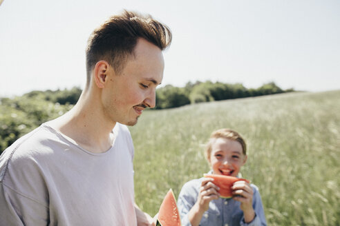 Glücklicher junger Mann und Junge auf einem Feld, die Wassermelonen essen - KMKF00289