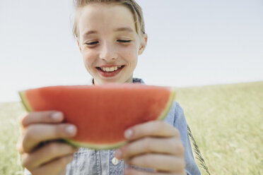 Glücklicher Junge auf einem Feld, der eine Wassermelone isst - KMKF00291
