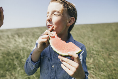 Junge auf einem Feld, der eine Wassermelone isst, lizenzfreies Stockfoto