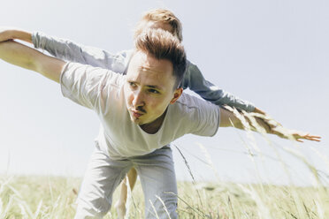 Young man and boy in a field pretending to fly - KMKF00307