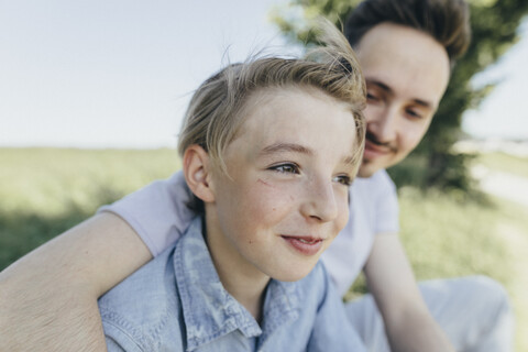 Porträt eines jungen Mannes, der einen lächelnden Jungen auf einem Feld umarmt, lizenzfreies Stockfoto