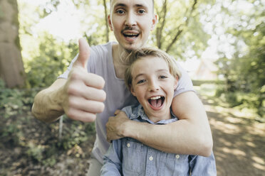 Portrait of happy young man embracing boy on forest path - KMKF00324