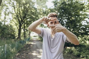 Junger Mann macht einen Fingerrahmen auf einem Waldweg - KMKF00331