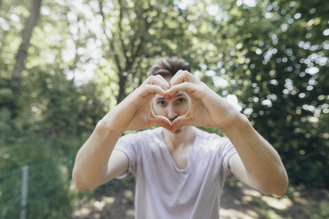 Junger Mann macht ein Herz mit seinen Fingern auf einem Waldweg, lizenzfreies Stockfoto