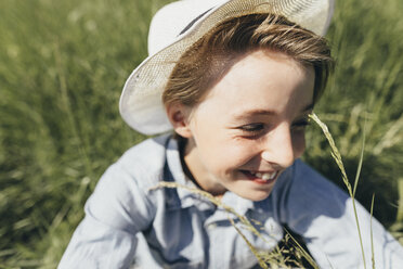 Glücklicher Junge mit Hut auf einem Feld sitzend - KMKF00339