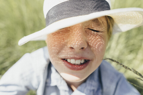 Junge mit geschlossenen Augen, der einen Hut trägt und im Feld sitzt, lizenzfreies Stockfoto