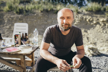 Portrait of smiling man with beard sitting outdoors - KMKF00343