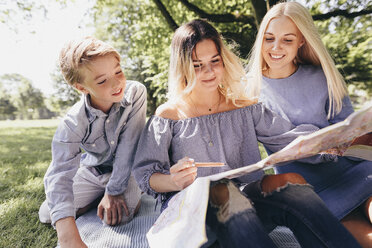 Zwei junge Frauen und ein Junge betrachten eine Karte in einem Park - KMKF00346