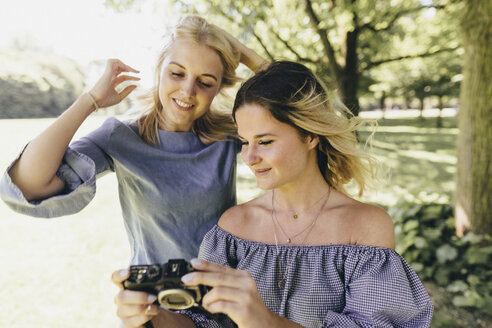 Zwei lächelnde junge Frauen mit altmodischer Kamera in einem Park - KMKF00350