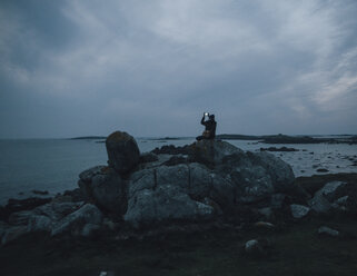 Frankreich, Bretagne, Landeda, Mann macht Handy-Foto an der Küste in der Abenddämmerung - GUSF00944