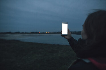 Frankreich, Bretagne, Landeda, Frau mit Mobiltelefon an der Küste in der Abenddämmerung - GUSF00947