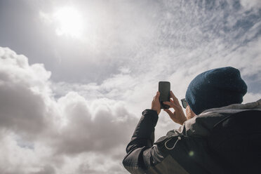 Mann hält Mobiltelefon unter sonnigem Himmel mit Wolken hoch - GUSF00950