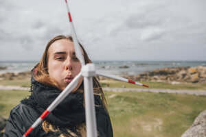 Frankreich, Bretagne, Meneham, junge Frau mit Miniatur-Windrad an der Küste - GUSF00961