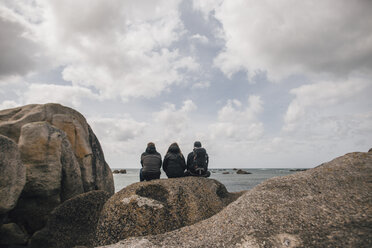 Frankreich, Bretagne, Meneham, Freunde sitzen auf einer Felsformation an der Küste - GUSF00962