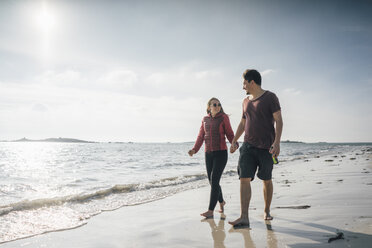 Frankreich, Bretagne, Landeda, Paar geht Hand in Hand am Strand spazieren - GUSF00964