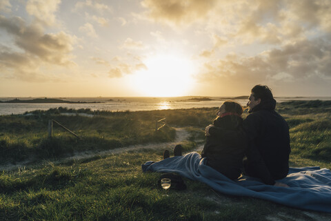 France, Brittany, Landeda, couple sitting at the coast at sunset stock photo