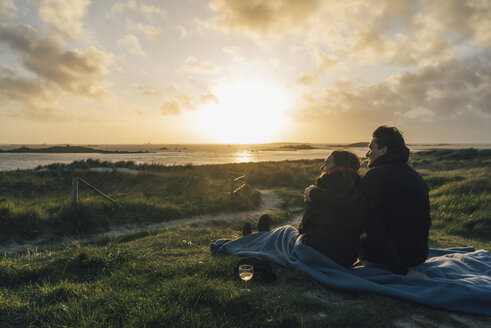 Frankreich, Bretagne, Landeda, Paar sitzt bei Sonnenuntergang an der Küste - GUSF00969