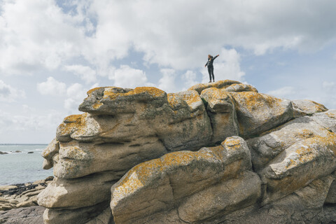 Frankreich, Bretagne, Meneham, Frau steht auf Felsformation an der Küste, lizenzfreies Stockfoto