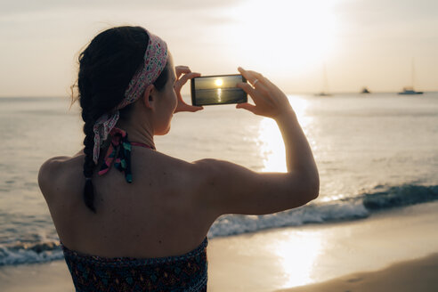 Thailand, Koh Lanta, Frau am Strand beim Fotografieren mit Handy bei Sonnenuntergang - GEMF02053