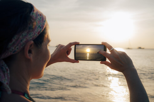 Thailand, Koh Lanta, Frau fotografiert mit Handy bei Sonnenuntergang - GEMF02054