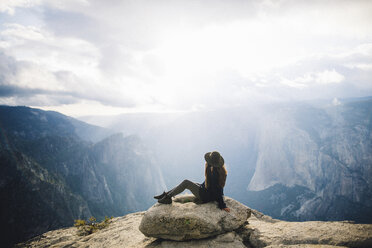 Young woman sitting at top of mountain, overlooking Yosemite National Park, California, USA - ISF08834