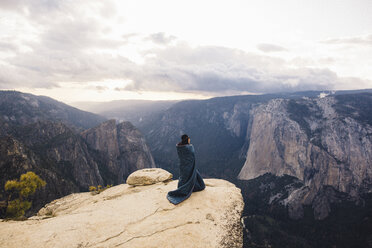 Junge Frau, in eine Decke eingewickelt, auf dem Gipfel eines Berges stehend, mit Blick auf den Yosemite National Park, Kalifornien, USA - ISF08835