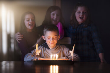 Boy surrounded by friends looking at birthday cake smiling - ISF08879