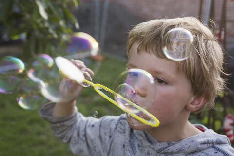 Nahaufnahme eines Jungen, der im Hinterhof mit einem Zauberstab Seifenblasen bläst, lizenzfreies Stockfoto