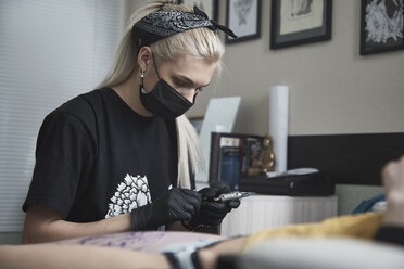 Tattoo artist preparing machine while sitting by customer at studio - FSIF03021