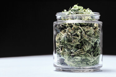 Marijuana leaves in glass jar on table against black background - FSIF03023