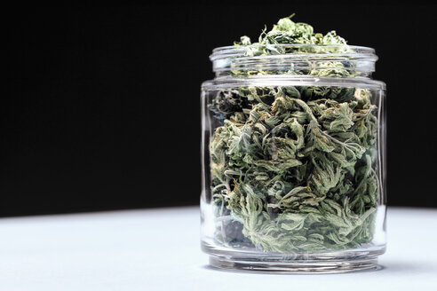Marihuana-Blätter in Glasgefäß auf Tisch vor schwarzem Hintergrund - FSIF03023