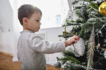 Side view of boy standing by Christmas tree at home - FSIF03039