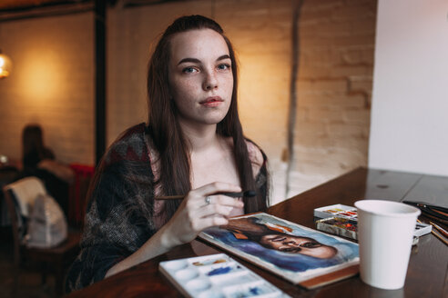 Porträt einer schönen jungen Frau, die bei einem Gemälde auf dem Tisch eines Cafés sitzt - FSIF03055