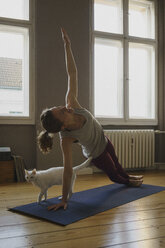 Full length of woman practicing side plank pose on exercise mat by cat at home - FSIF03057