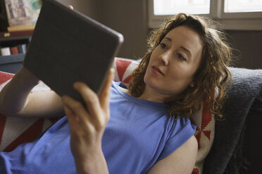 Frau auf dem Sofa liegend, während sie ein digitales Tablet zu Hause benutzt - FSIF03062