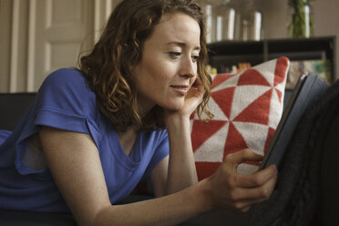 Woman using digital tablet on sofa at home - FSIF03063