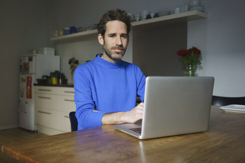 Porträt eines selbstbewussten Mannes, der mit einem Laptop am Tisch in der Küche sitzt - FSIF03067