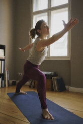 Full length of woman practicing warrior 2 position on exercise mat at home - FSIF03069